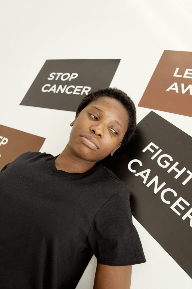 Black woman standing against a wall with cancer advocacy placards, promoting awareness and strength.