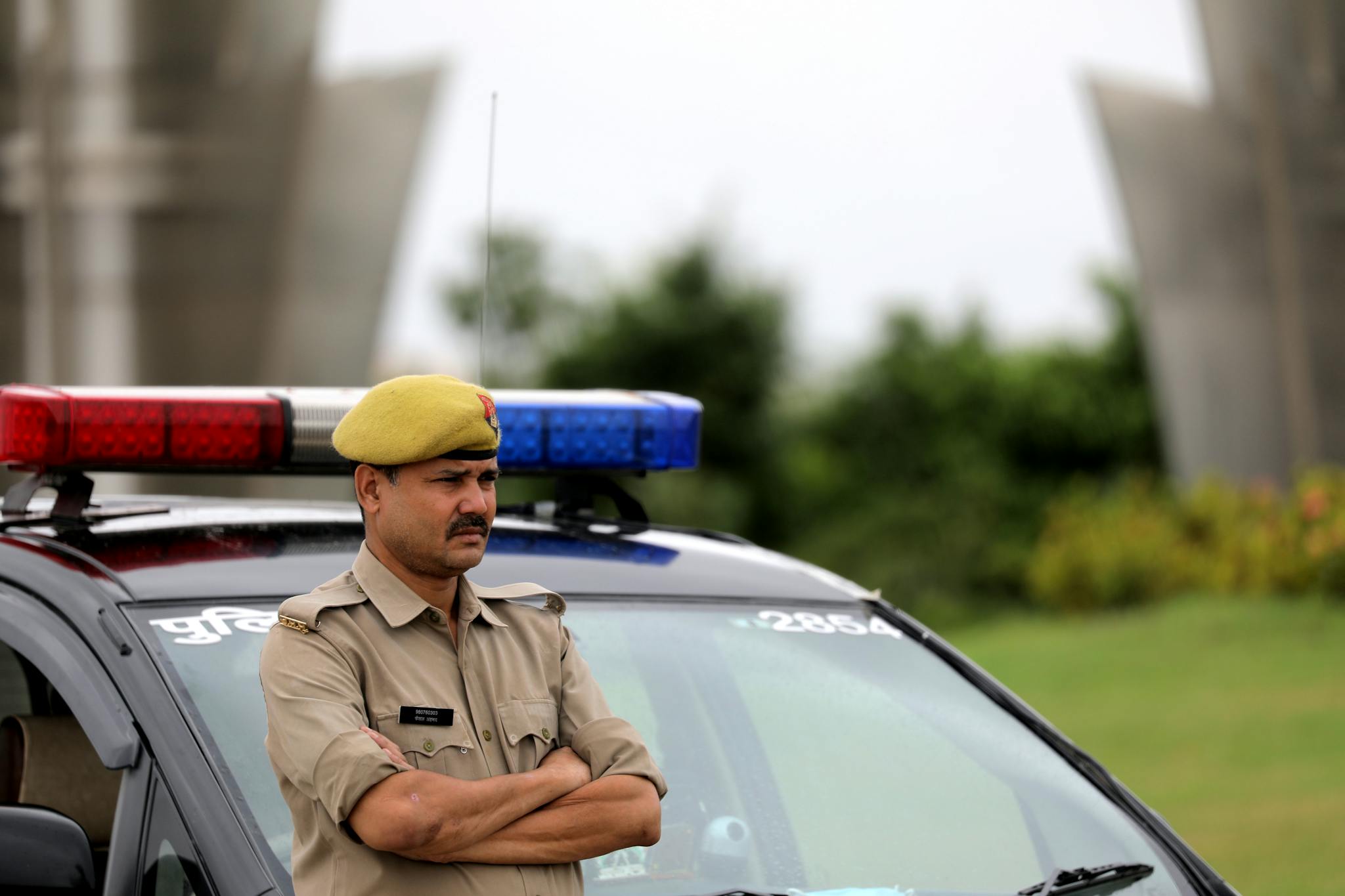 Indian police officer with arms crossed standing by a patrol car outdoors, showcasing authority and law enforcement presence.
